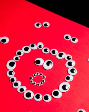 Kırmızı arka plandaki diğer gözlerin etrafındaki oyuncak gözlerden gelen şaşkın gülen yüz.