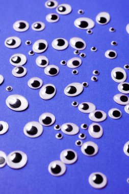 Farklı boyutlarda oyuncak gözler, mor bir arka plana saçılmış.