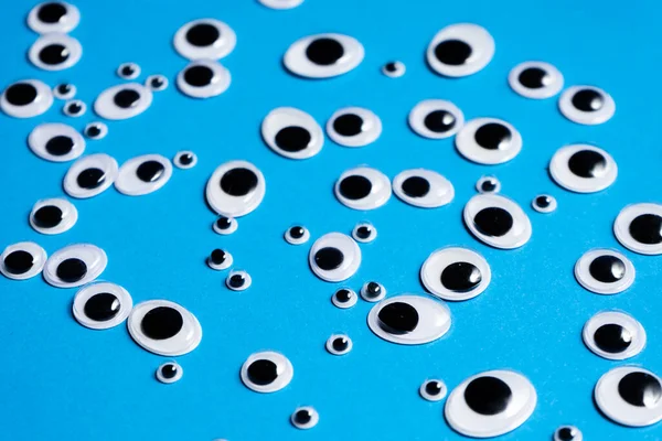 Farklı boyutlarda oyuncak gözler mavi arka plana saçılmış.