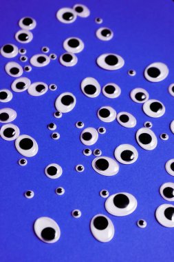 Farklı boyutlarda oyuncak gözler, mor bir arka plana saçılmış.