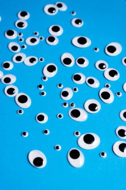 Farklı boyutlarda oyuncak gözler mavi arka plana saçılmış.