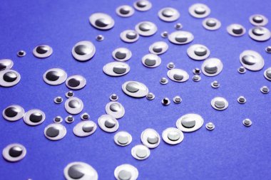 Farklı boyutlarda oyuncak gözler, mor bir arka plana saçılmış.