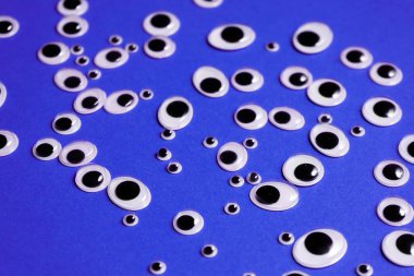 Farklı boyutlarda oyuncak gözler, mor bir arka plana saçılmış.