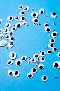 Farklı boyutlarda oyuncak gözler mavi arka plana saçılmış.