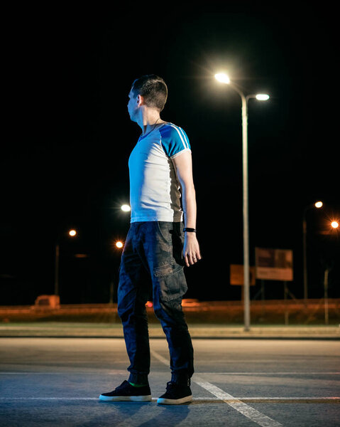 Парень стоит в парке, под фонарями.