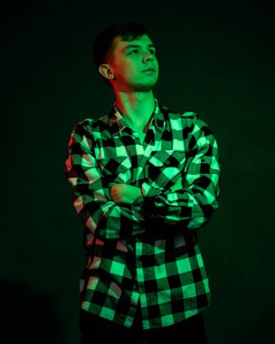 Stüdyoda ekose gömlekli genç bir adam. Siyah arka planda kırmızı ve yeşil ışık var.