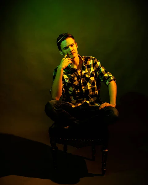 Killen i rutig skjorta med en kam i håret sitter på en stol. med gult och grönt ljus — Stockfoto