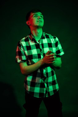 Stüdyoda ekose gömlekli genç bir adam. Siyah arka planda kırmızı ve yeşil ışık var.