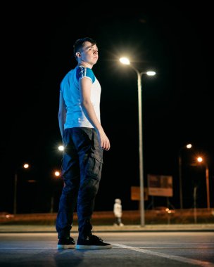 Adam parkta duruyor, fenerlerin altında.