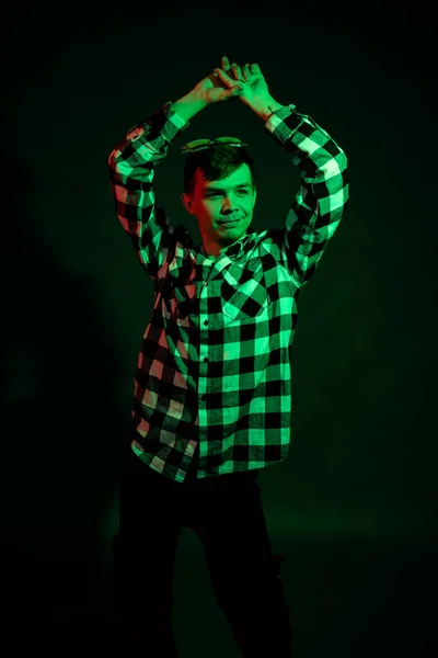 En ung man i rutig skjorta i en studio med rött och grönt ljus på svart bakgrund — Stockfoto