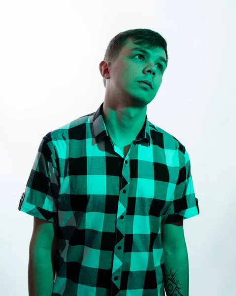 Porträt eines jungen Mannes, der von einem grünen Licht beleuchtet wird, vor weißem Hintergrund Stockbild