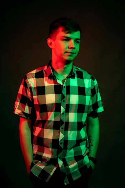 En ung man i rutig skjorta i en studio med rött och grönt ljus på svart bakgrund — Stockfoto
