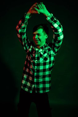 Stüdyoda ekose gömlekli genç bir adam. Siyah arka planda kırmızı ve yeşil ışık var.