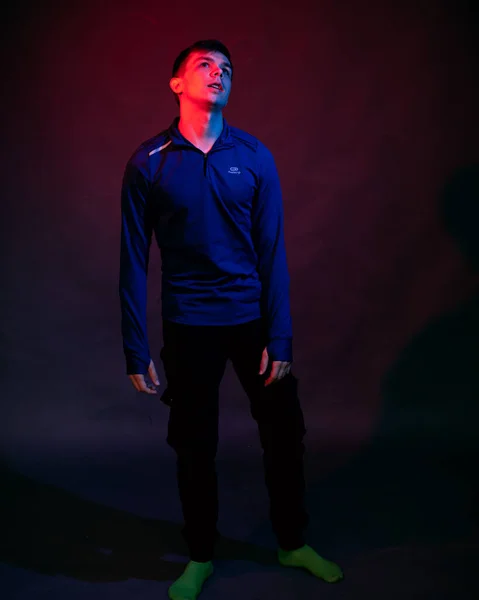 En ung man i blå blus i studion med blått och rött ljus — Stockfoto