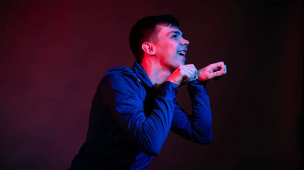 En ung man i blå blus i studion med blått och rött ljus — Stockfoto