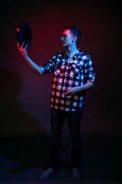En kille i rutig skjorta med rött och blått ljus i studion på svart bakgrund — Stockfoto