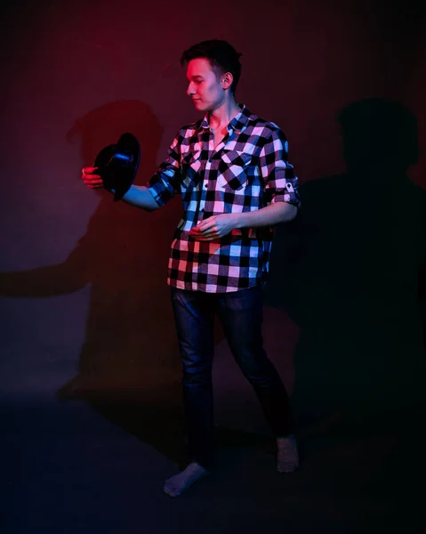 Um cara em uma camisa xadrez com iluminação vermelha e azul no estúdio em um fundo preto — Fotografia de Stock