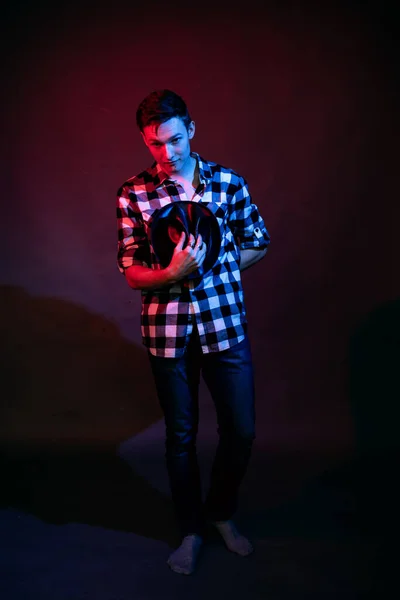 En kille i rutig skjorta med rött och blått ljus i studion på svart bakgrund — Stockfoto