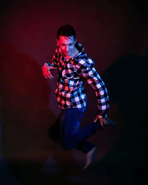 Un tipo con una camisa a cuadros con iluminación roja y azul en el estudio sobre un fondo negro —  Fotos de Stock