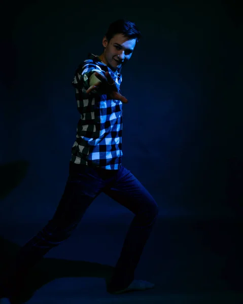 En ung man i en studio på en mörk bakgrund med ett flerfärgat ljus — Stockfoto