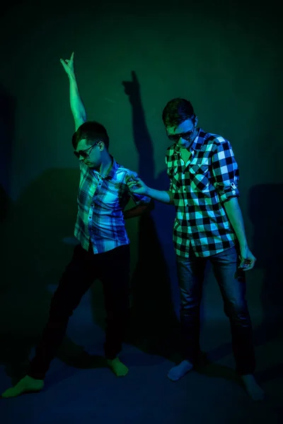 Två unga män i rutiga skjortor dansar i studion med flerfärgat ljus — Stockfoto
