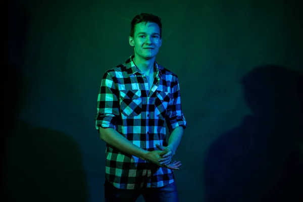 En ung man i en studio på en mörk bakgrund med ett flerfärgat ljus — Stockfoto