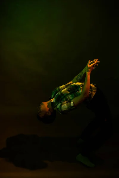 Killen i rutig skjorta dansar, upplyst av orange och grönt ljus — Stockfoto