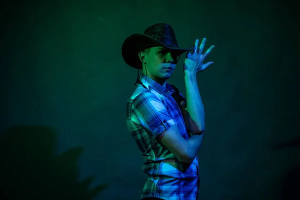 En kille i cowboyhatt och rutig skjorta i en studio med blått och grönt ljus — Stockfoto