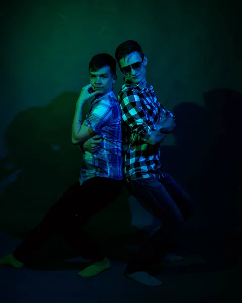 Deux jeunes hommes en chemises à carreaux dansent en studio avec une lumière multicolore — Photo