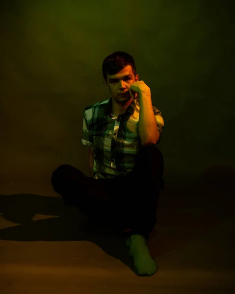 En ung man sitter på golvet. belyst av flerfärgat ljus — Stockfoto