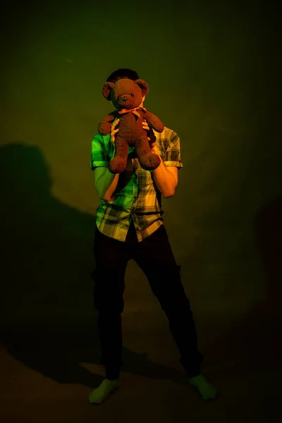 Der Kerl spielt mit einem Teddybär, beleuchtet von gelbem und grünem Licht — Stockfoto