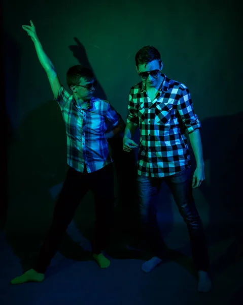 Två unga män i rutiga skjortor dansar i studion med flerfärgat ljus — Stockfoto