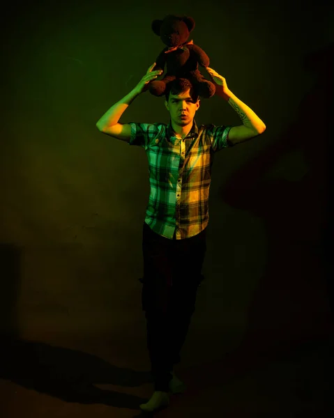 El tipo juega con un osito de peluche, iluminado por la luz amarilla y verde — Foto de Stock