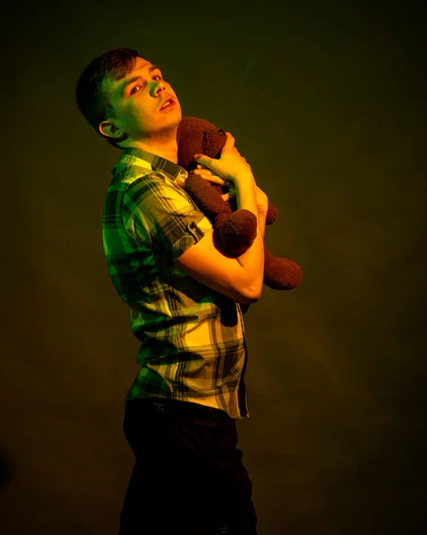 Le gars joue avec un ours en peluche, illuminé par la lumière jaune et verte — Photo