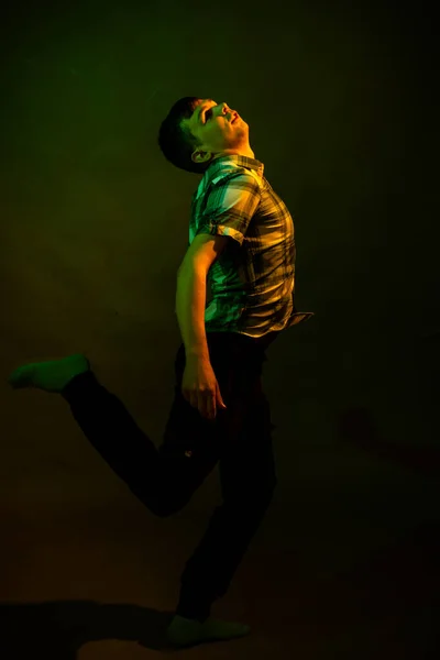 El tipo de la camisa a cuadros baila, iluminado por la luz naranja y verde —  Fotos de Stock