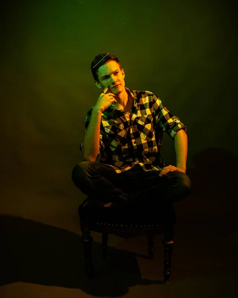Un joven se sienta sobre un fondo oscuro iluminado por la luz verde y amarilla como en una película — Foto de Stock