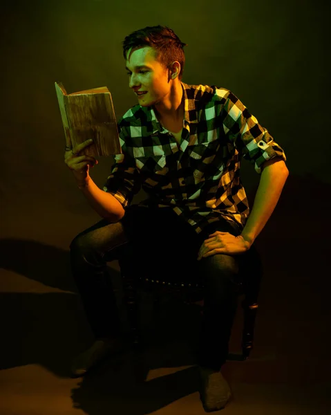 Un gars en chemise à carreaux lit un livre éclairé par une lumière multicolore — Photo