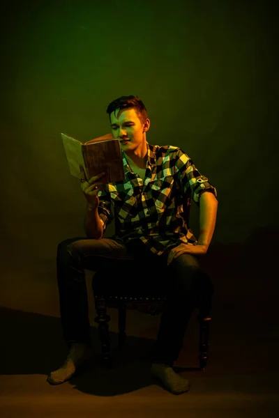 Un tipo con una camisa a cuadros lee un libro iluminado por luz multicolor — Foto de Stock