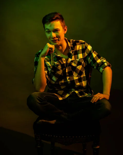 Un jeune homme assis sur un fond sombre éclairé par la lumière verte et jaune comme dans un film — Photo