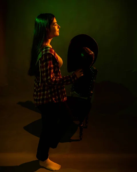 Ein Mädchen im karierten Hemd mit Cowboyhut, angestrahlt von buntem Licht — Stockfoto