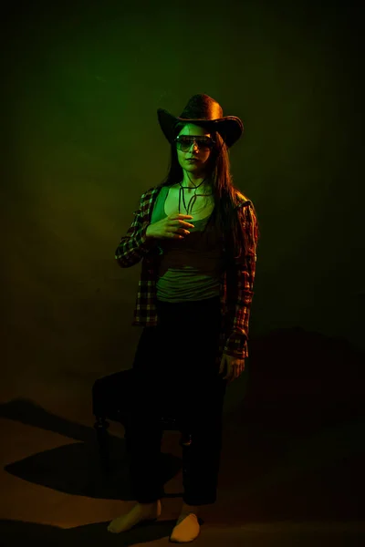 Une fille en chemise à carreaux avec un chapeau de cow-boy illuminé par une lumière multicolore — Photo