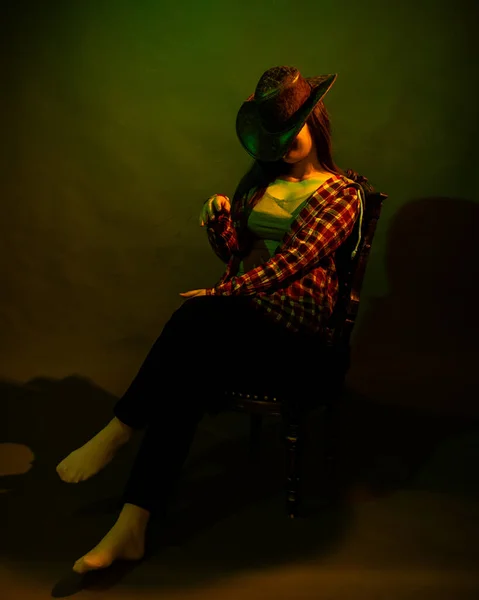 The girl sits on a black chair illuminated by multicolored light — Stock Photo, Image