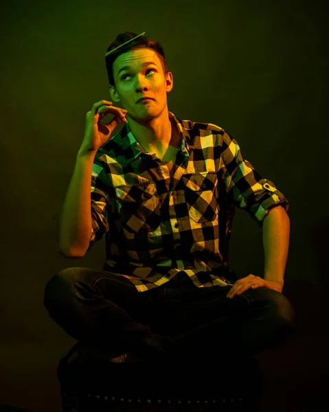 Un jeune homme assis sur un fond sombre éclairé par la lumière verte et jaune comme dans un film — Photo