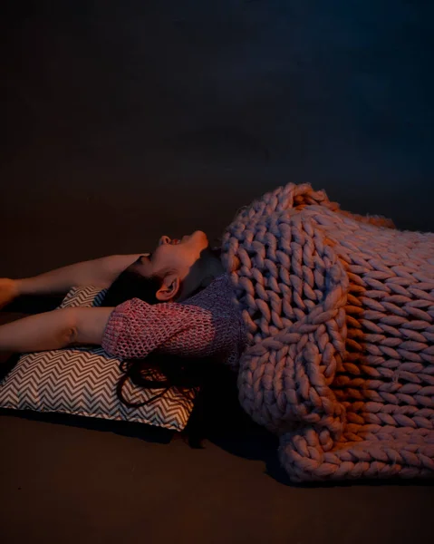 The girl lies on the floor, covered with a pink plaid, illuminated by a warm light — Stock Photo, Image