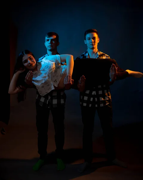 Two guys in a plaid shirt are holding a girl on a dark background in a studio with multicolored light — Photo