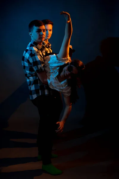 Two guys in a plaid shirt are holding a girl on a dark background in a studio with multicolored light — Photo