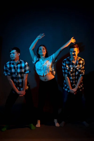Two guys in plaid shirts and a girl dancing on a dark background, illuminated by blue and yellow light — Photo