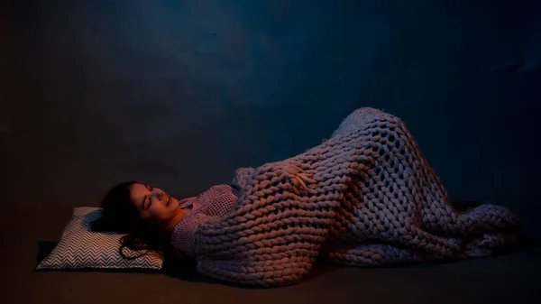 The girl lies on the floor, covered with a pink plaid, illuminated by a warm light — Stock Photo, Image
