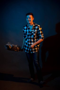 A guy in a plaid shirt with a dust brush on a dark background illuminated by blue and yellow light