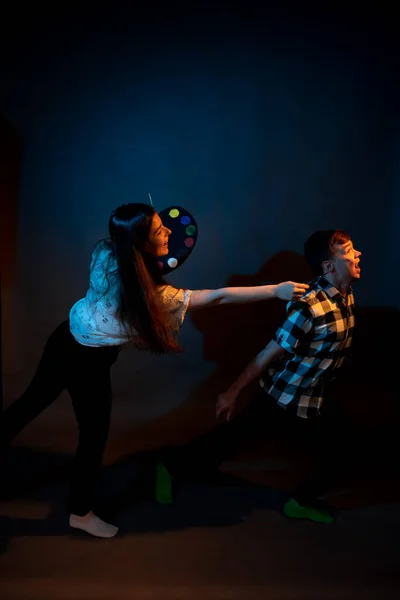 A girl paints a guy in the studio on a dark background illuminated by multicolored light — Photo